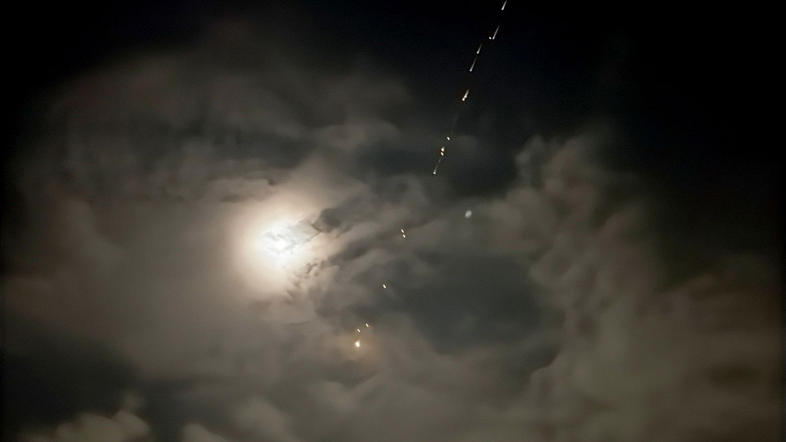 A cloudy night sky with flashes of light in a line