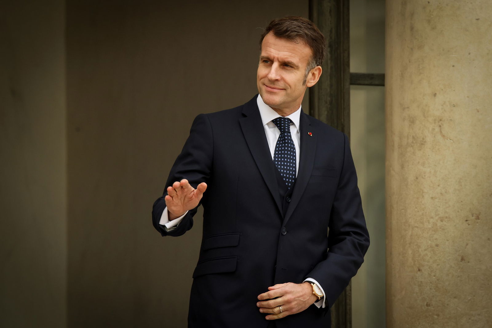 French President Emmanuel Macron standing and waving with his right hand. 