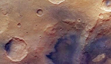 A high-resolution image of the Martian surface shows several impact craters of varying sizes on a dusty, reddish-brown landscape with some shadowed and rough textured areas.