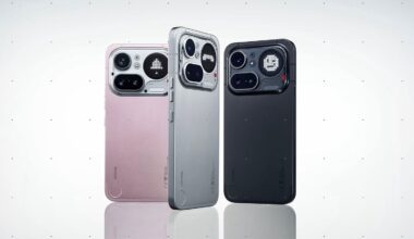 Three smartphones are standing upright side by side, displayed in pink, silver, and black colors. Each phone has a distinctive large camera module with multiple lenses and sensors on a minimalist back design.