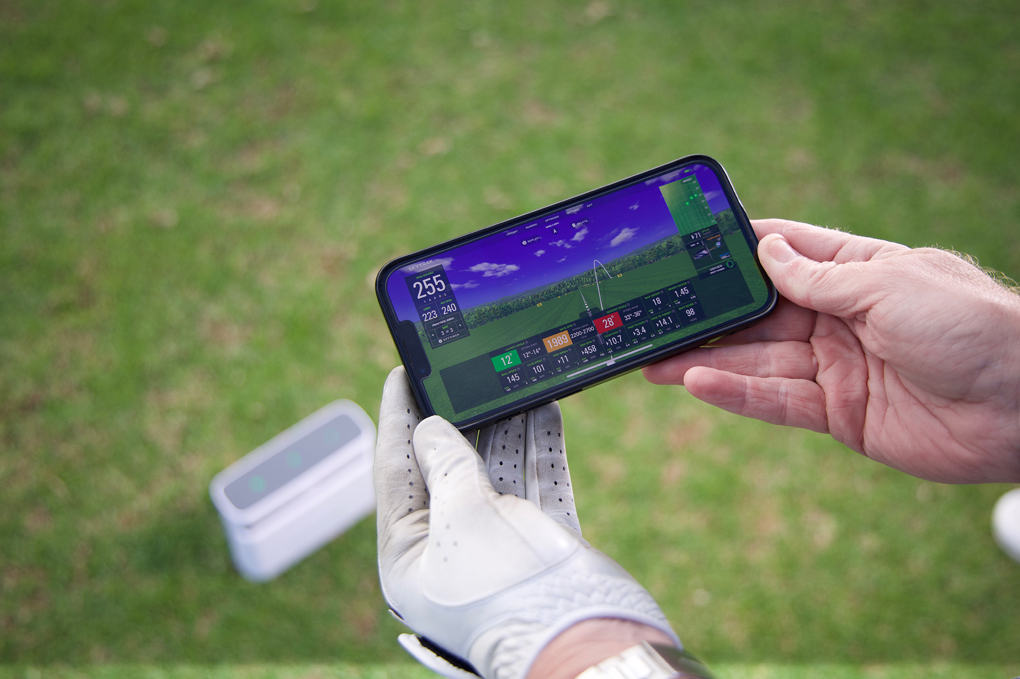 Ged Walters using a distance tracking device to measure clubhead speed, with data visible on his mobile phone screen