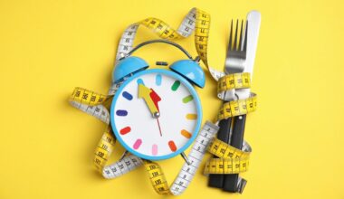 Alarm clock, measuring tape and cutlery on yellow background, flat lay
