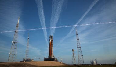A large orange and white rocket sits on a launch pad with streaks of white clouds behind it