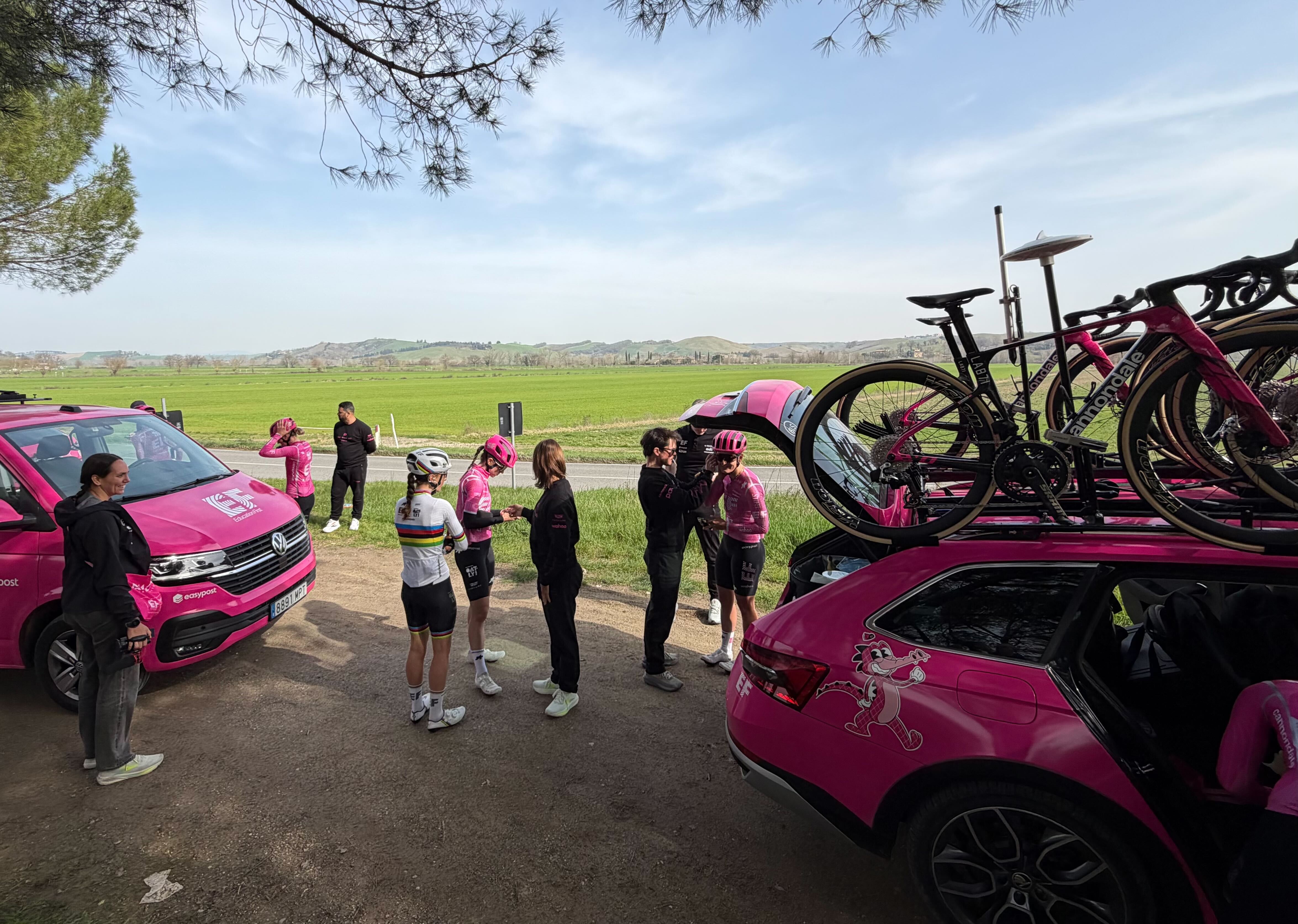 The EF-Oatly riders stand between two team cars preparing for their recon of Strade Bianche