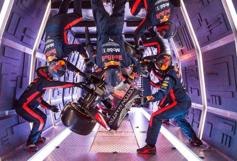 Red Bull Racing Formula 1 pit crew members perform a simulated pit stop in a zero-gravity environment, with tools and car parts floating as they work inside a futuristic, enclosed space.