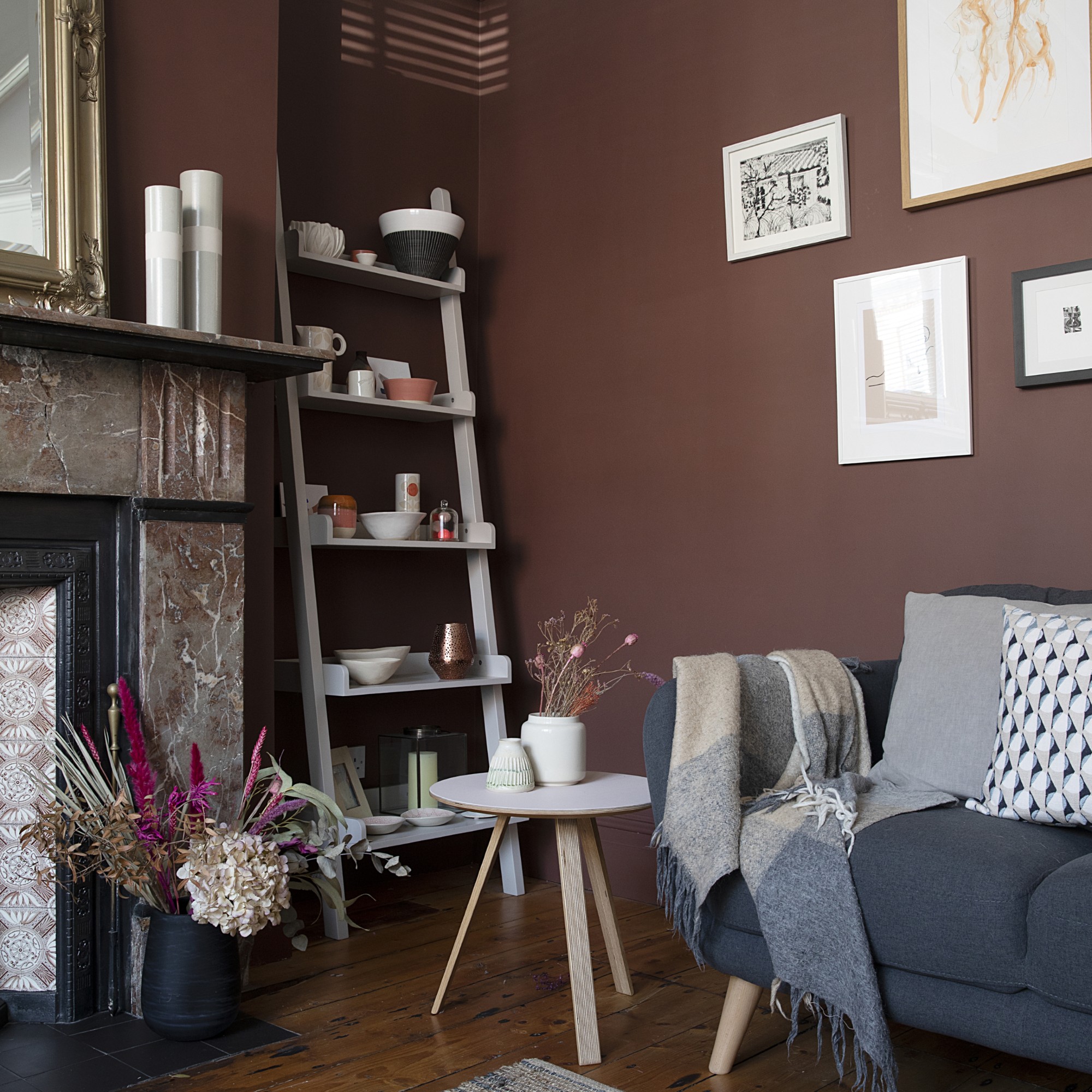 A living room painted in a chocolate brown shade with a marble fireplace and a dark grey sofa