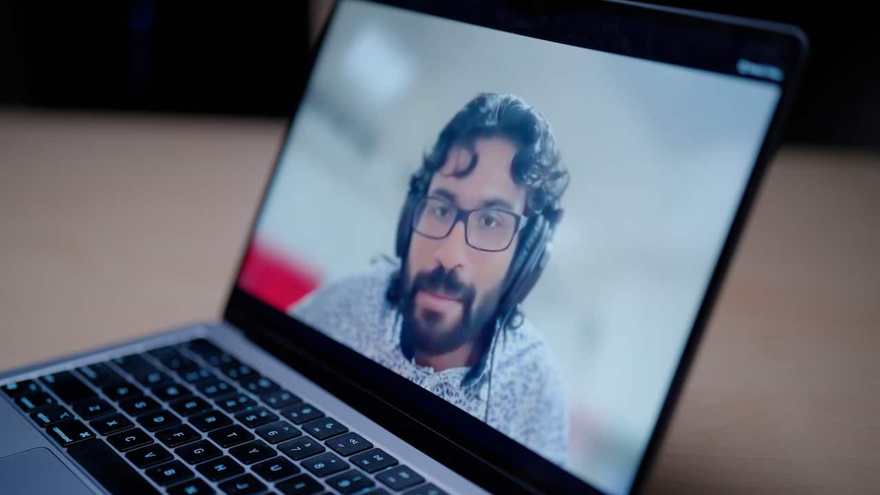 A laptop showing a man wearing headphones speaking on a video call