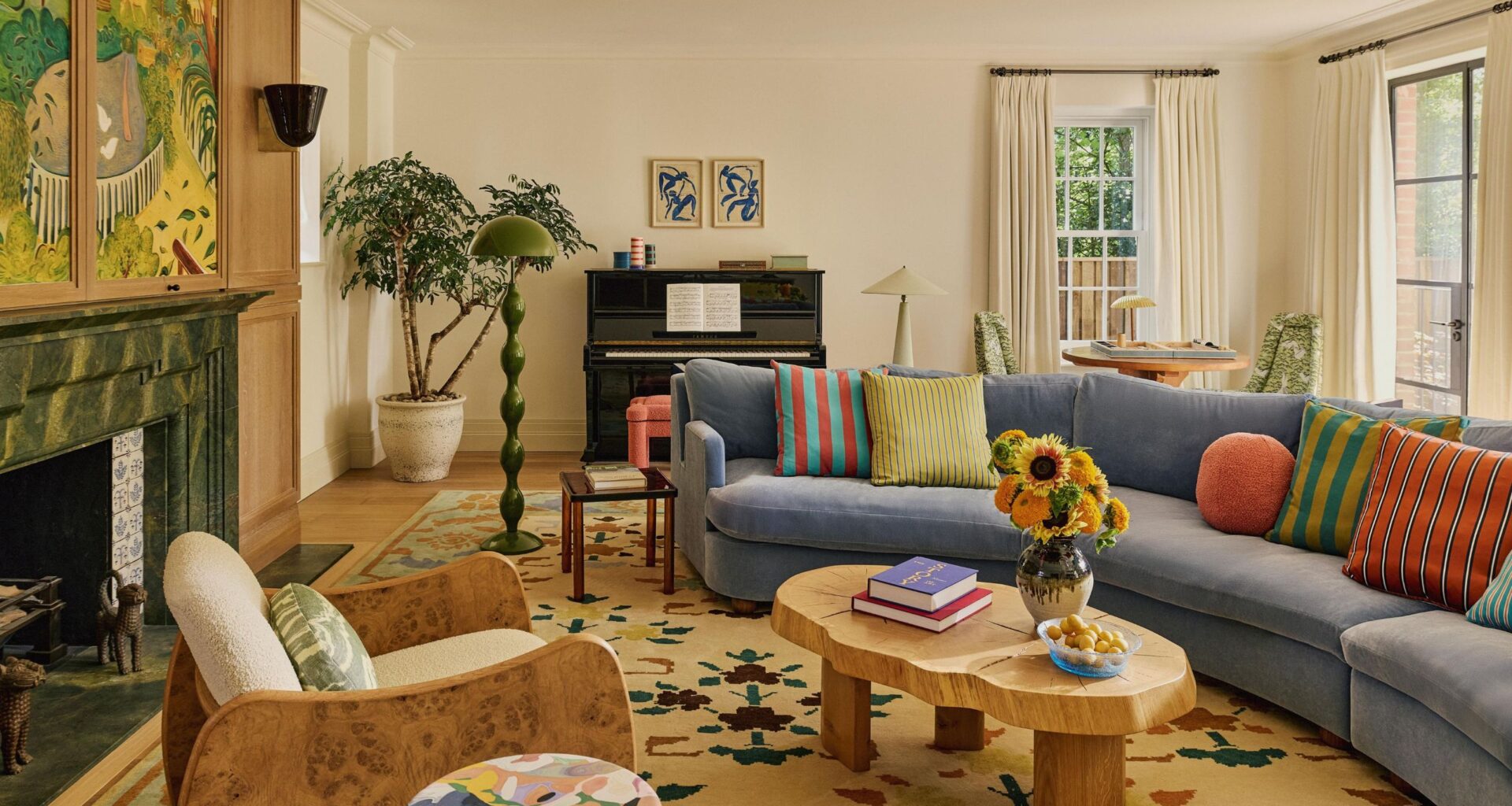 a warm neutral london living room centered around a large fireplace with large artwork hung above. a blue curved couch sits to the right, with a wooden coffee table and patterned rug