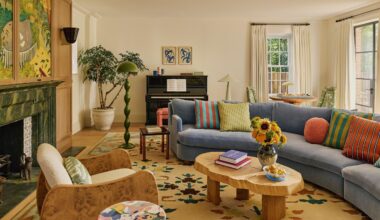 a warm neutral london living room centered around a large fireplace with large artwork hung above. a blue curved couch sits to the right, with a wooden coffee table and patterned rug