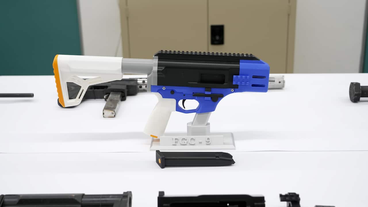 A plastic gun featuring a black and blue middle, white stock and white pistol grip sitting upright on a table