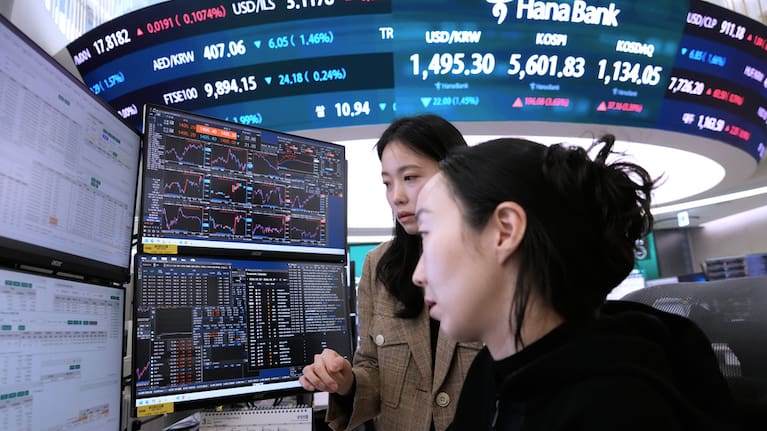 Currency traders watch monitors near a screen showing the Korea Composite Stock Price Index