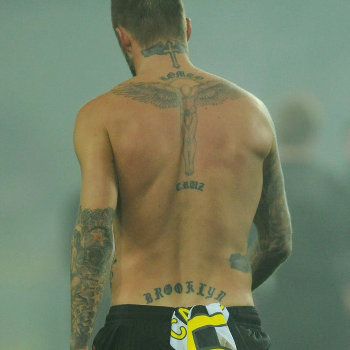 Shirtless athlete with tattoos on his back, holding a striped jersey on a foggy sports field