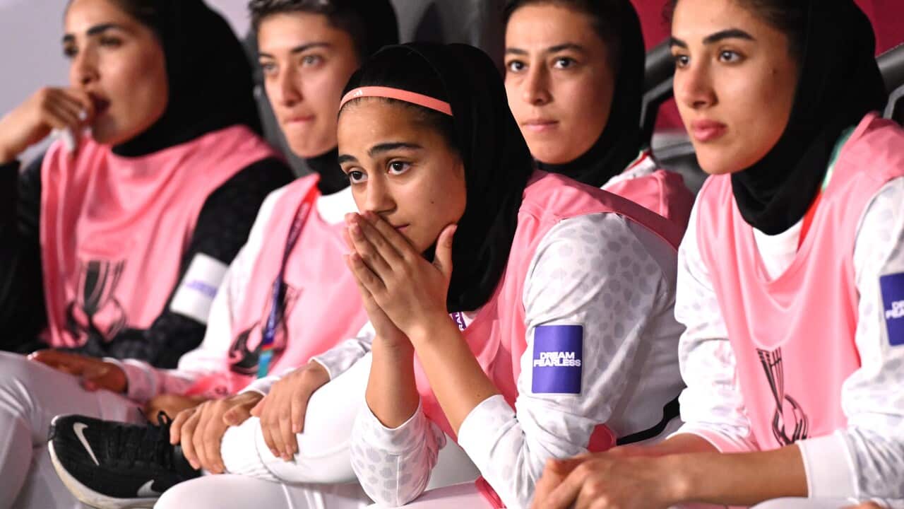 Iranian women's football players are sitting on the bench, watching the match with concerned expressions.