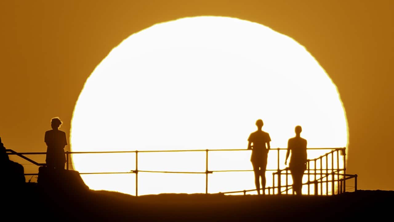 Silhouettes of people against a large, burning white sun in an orange sky.