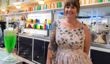Kylie Evans wearing a floral print dress stands behind the milk bar counter.