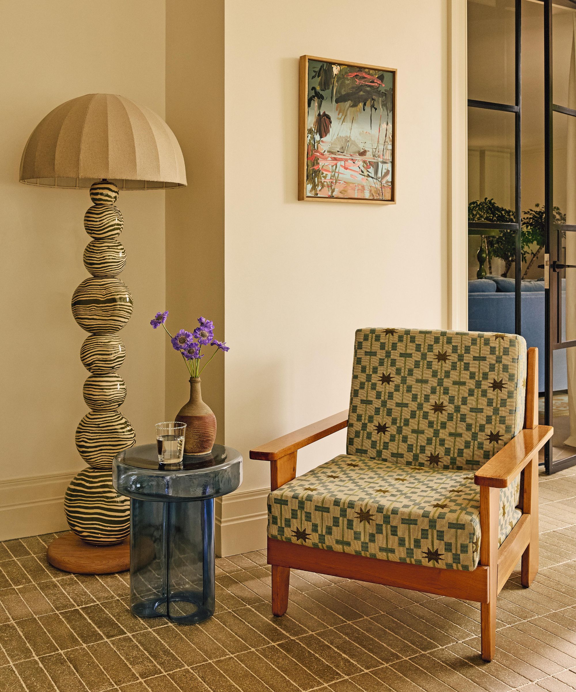 a vignette in a dining room with an armchair upholstered in a star print fabric, with a ceramic floor lamp with linen shade and a blue glass side table