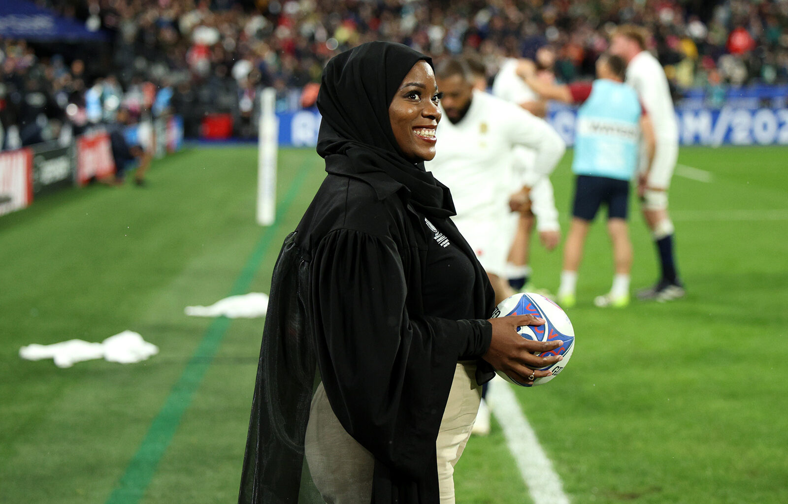 A photograph of a smiling Zainab Alema, waiting pitchside to present the match ball to the referee, ahead of the England v South Africa men