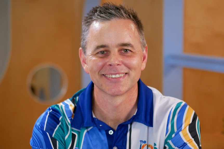 A white man with short hair sitting in an office space and smiling