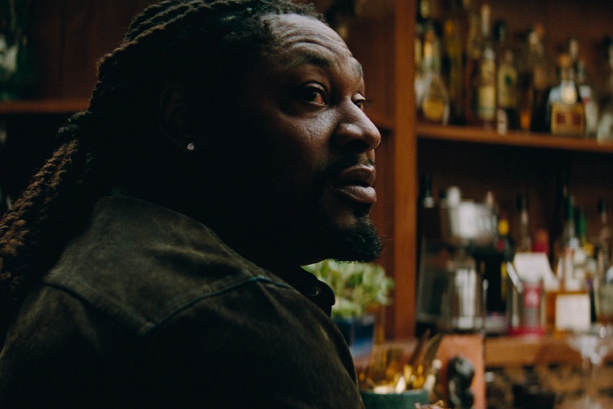Marshawn Lynch with long braided hair, side profile, sitting at a bar