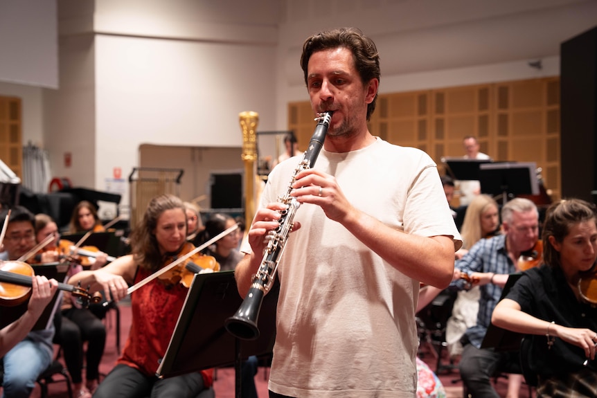 A clarinetist rehearsing a concerto with an orchestra behind him.