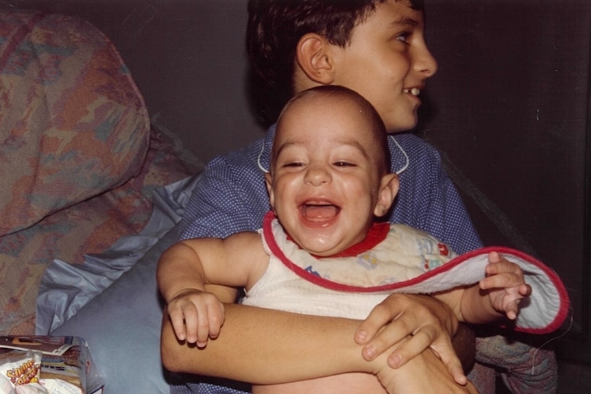 A 10-year-old boy wearing blue pyjamas holds a smiling baby, who is wearing a bib.