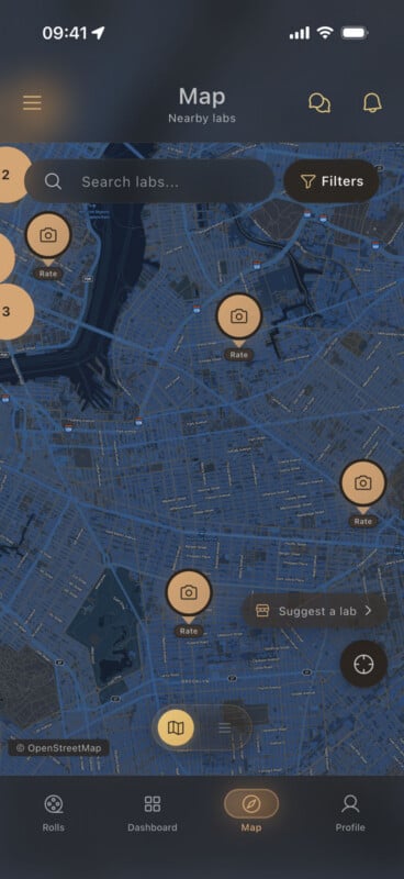 A smartphone screen displays a map interface for finding nearby photo labs, with various camera icons marking locations. Search, filter, and suggestion options are visible at the top. Navigation icons line the bottom of the screen.