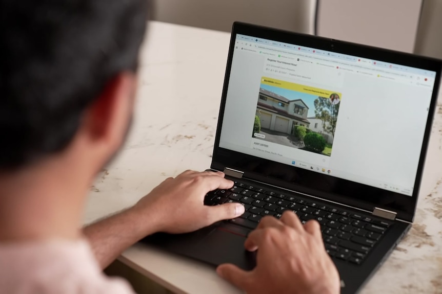 A man pictured from the back looking at a webpage on his laptops as he types