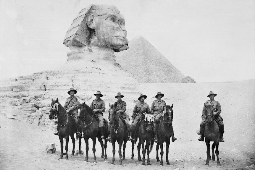 A black and white photo of uniformed soldiers on horses, lined up in front of pyramids in Egypt.