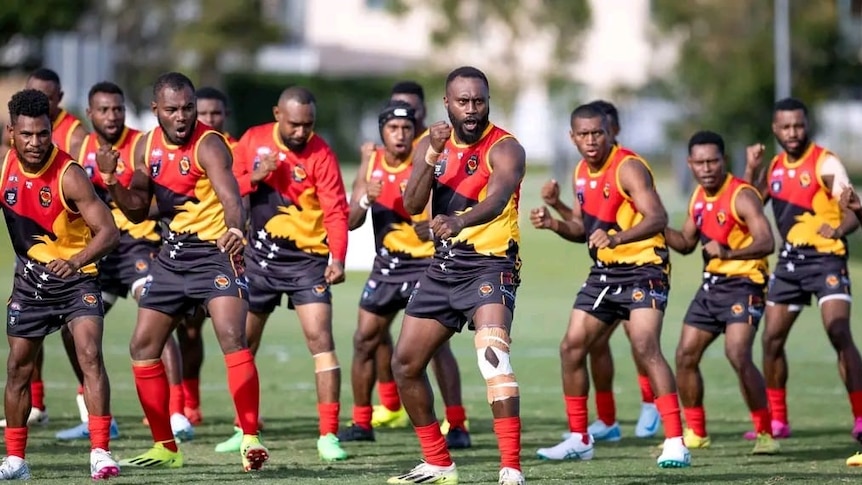 A group of PNG men wearing PNG AFL uniforms stand on a field in pre-match challenge stances