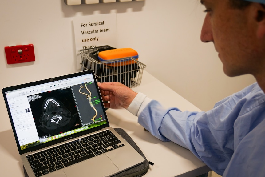 Man in blue scrubs looking at a laptop screen