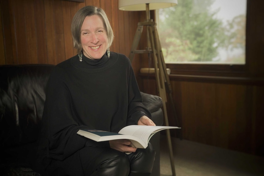 Portrait of UTAS Tourism academic Anne Hardy holding a book