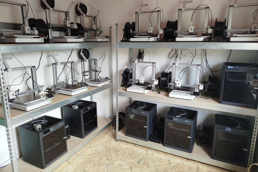 3D printers on shelves cover the walls of a small room