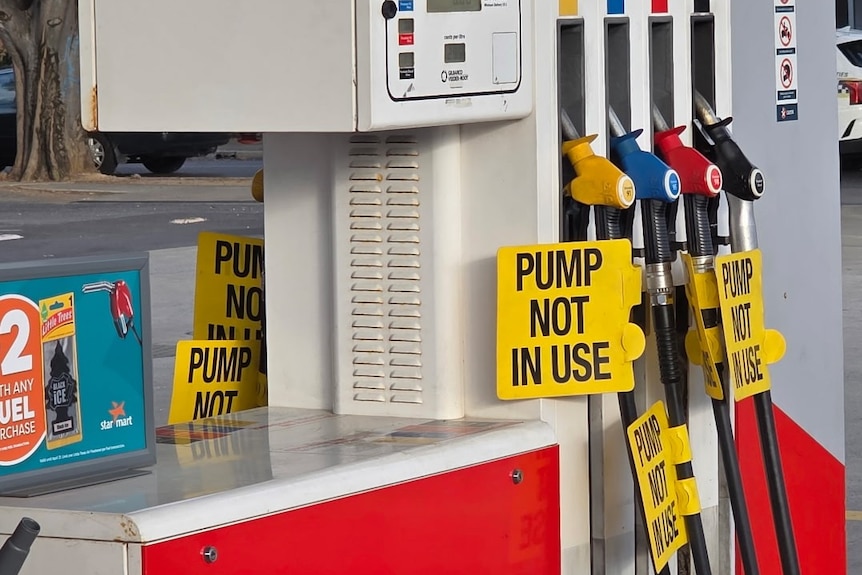Tags saying 'Pump not in use' tie around some nozzles at a fuel pump