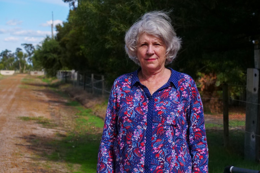 Woman in bright shirts stands off to the side of a road.