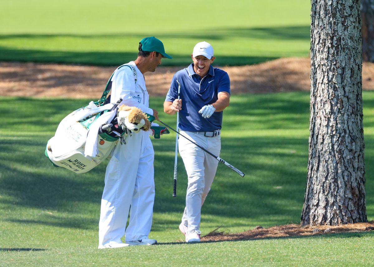 Rory McIlroy of Northern Ireland gives his club to his caddie Harry Diamond as he emerges from the trees laughing after he had played a brilliant second shot recovery on the seventh hole