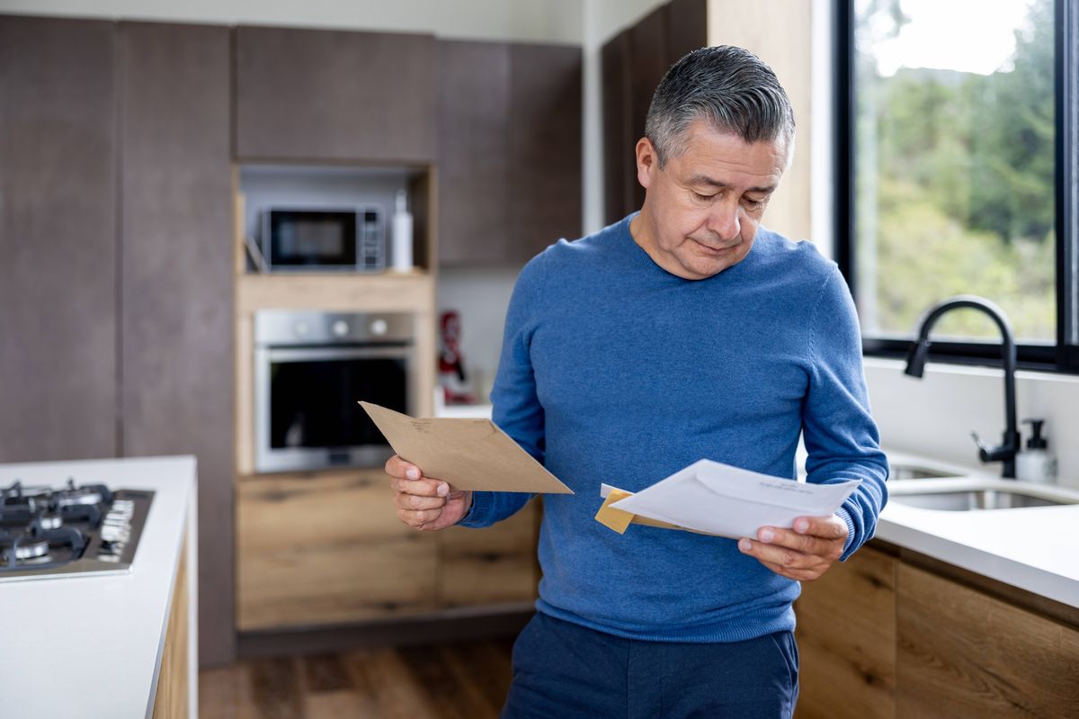 Latin American man at home checking his mail and holding envelopes - Lifestyle concepts