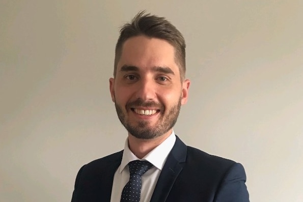 A headshot of a young man in a suit and tie smiling 