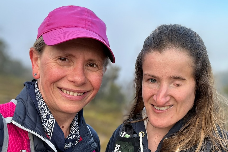 Two smiling women on a bushy slope.