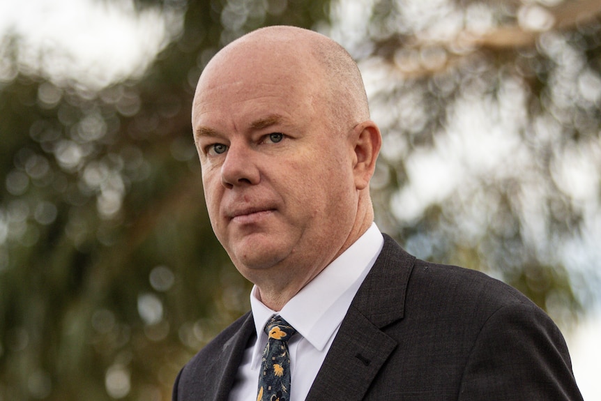 Simon Patterson, the husband of Erin Patterson, walks outside. He is wearing a suit.