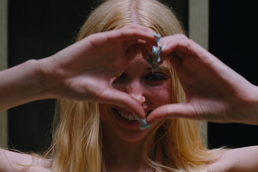 A blond woman makes a love heart with her hands