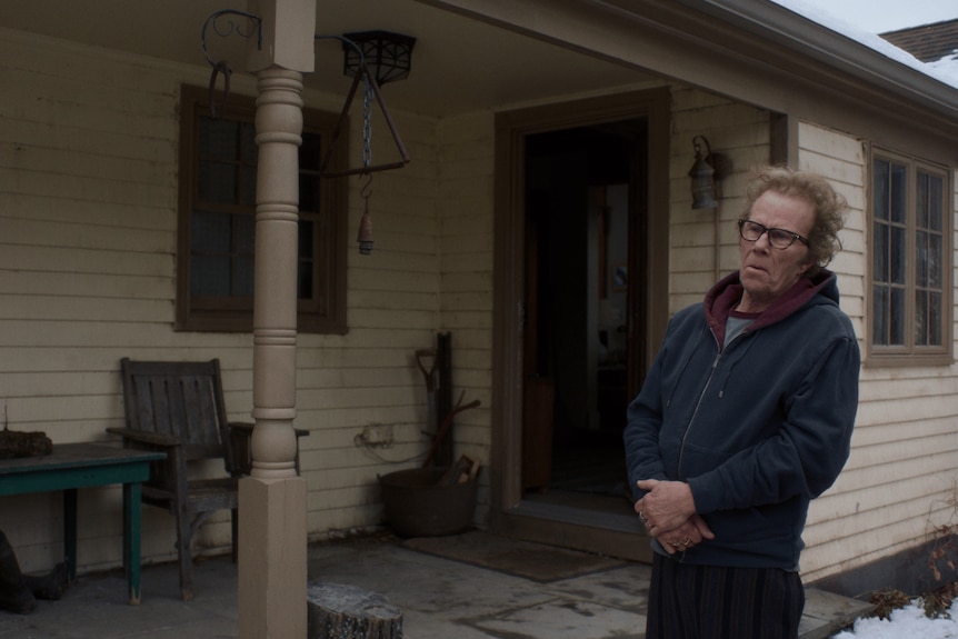 A man stands outside of a house, looking at something off screen.