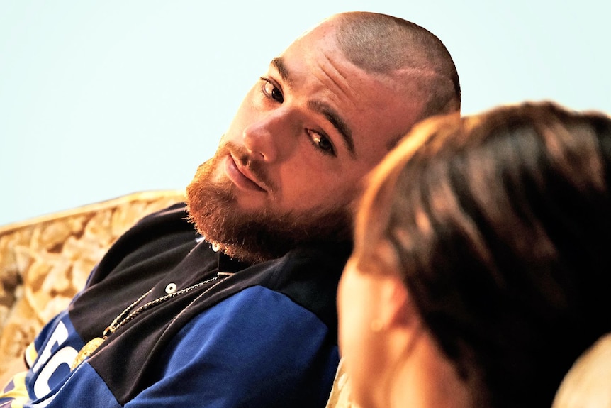 A man looks at a woman while they both sit on a couch