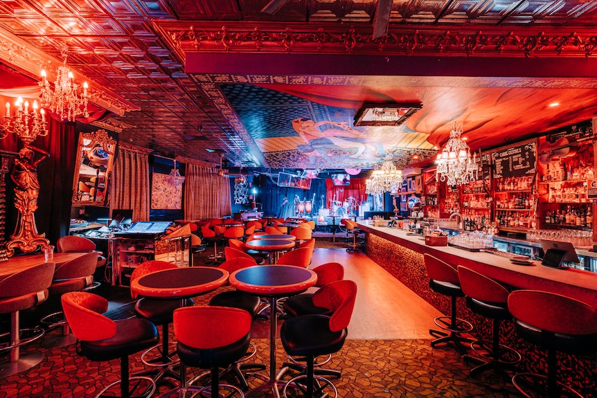 A venue shown in red lighting. there is a stage and bar. 