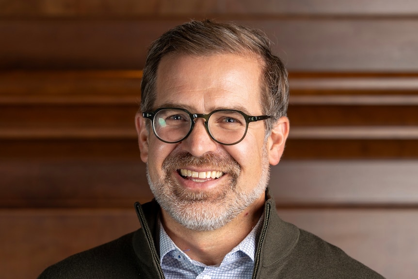 close up of a mans face with brown hair and reading glasses.