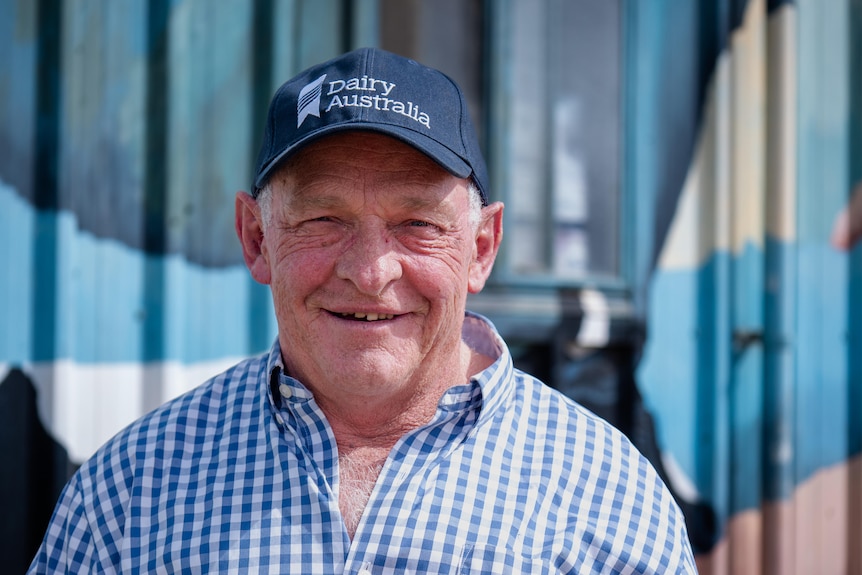 A man in a blue checked shirt and a navy blue hat standing in front of a colourful wall