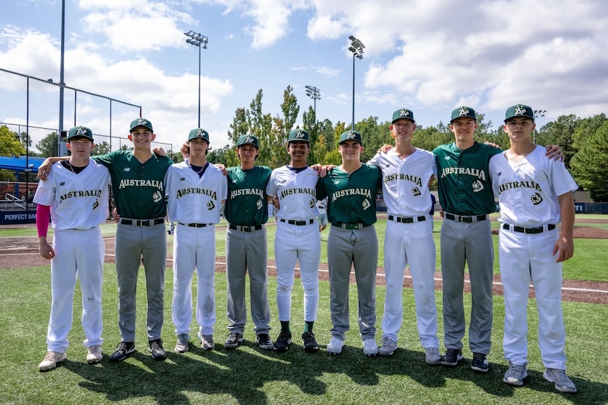 A group of teenagers stand shoulder to shoulder wearing baseball uniforms