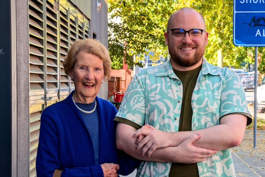 An elderly woman in blue holds the arm of her grandson.