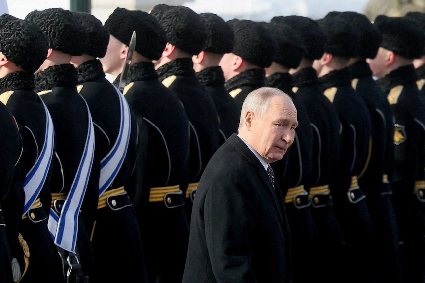 Vladimir Putin looks a bit tired as he walks past a row of soldiers.