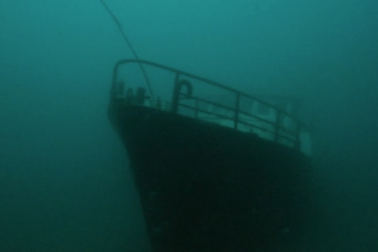 The bow of a submerged boat in cloudy green water.