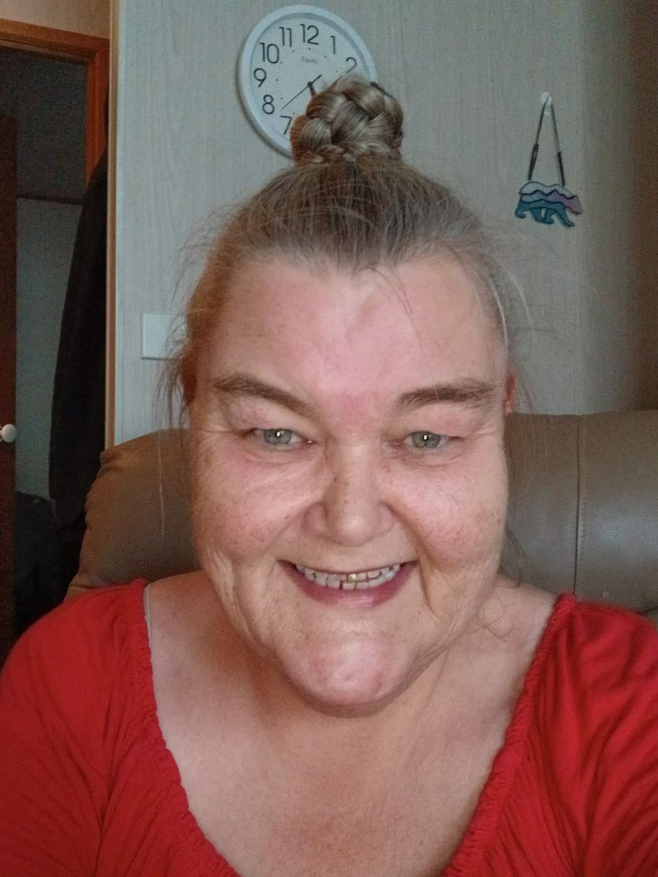 A woman with a grey bun and a red top smiles at the camera.
